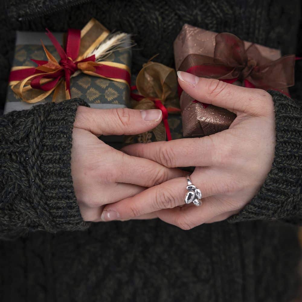 Handen i en mörk stickad tröja bär en handgjord ring i 925 sterling silver med fyra potatisformade delar